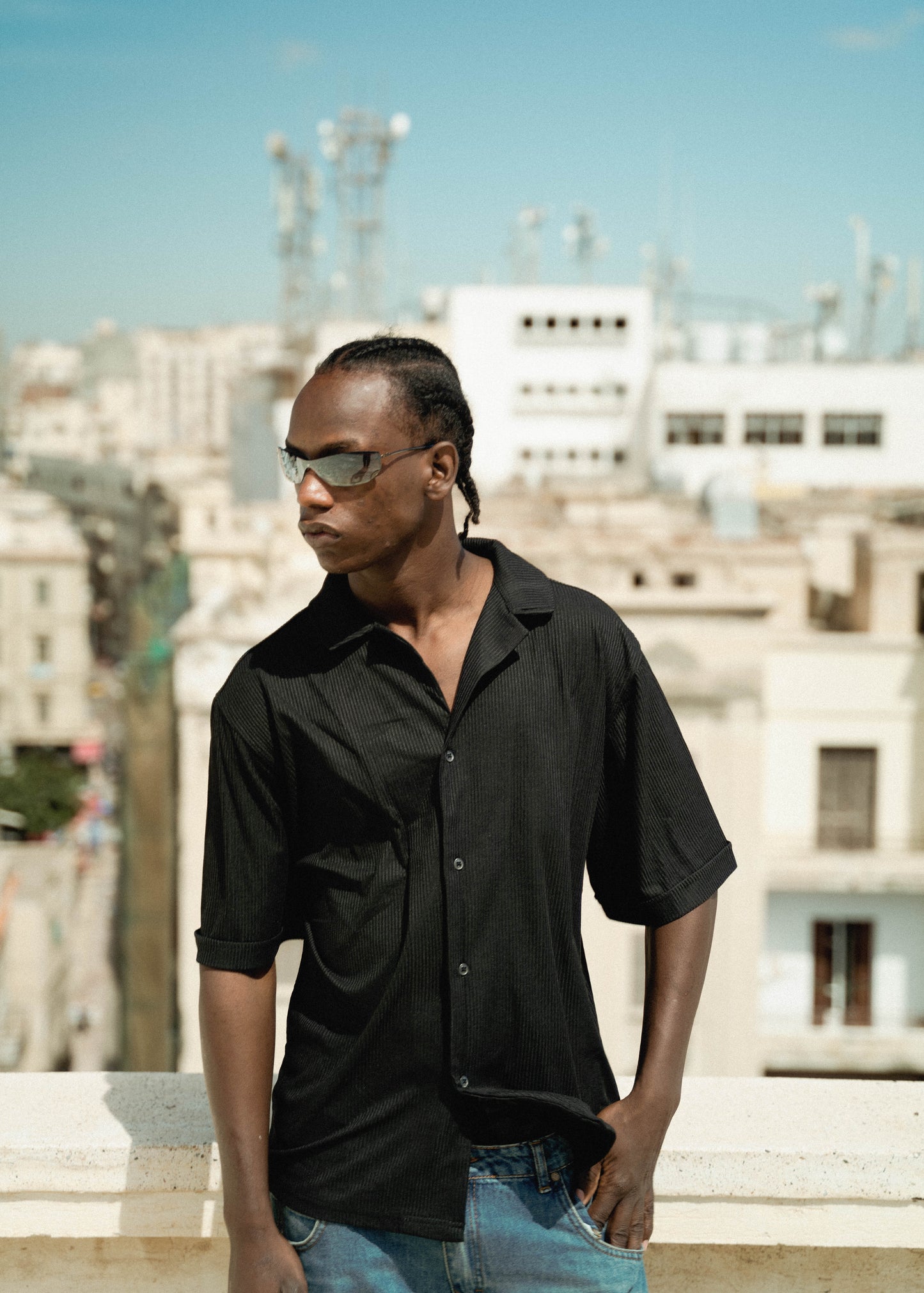 Man wearing sunglasses and a black shirt with a cityscape background
