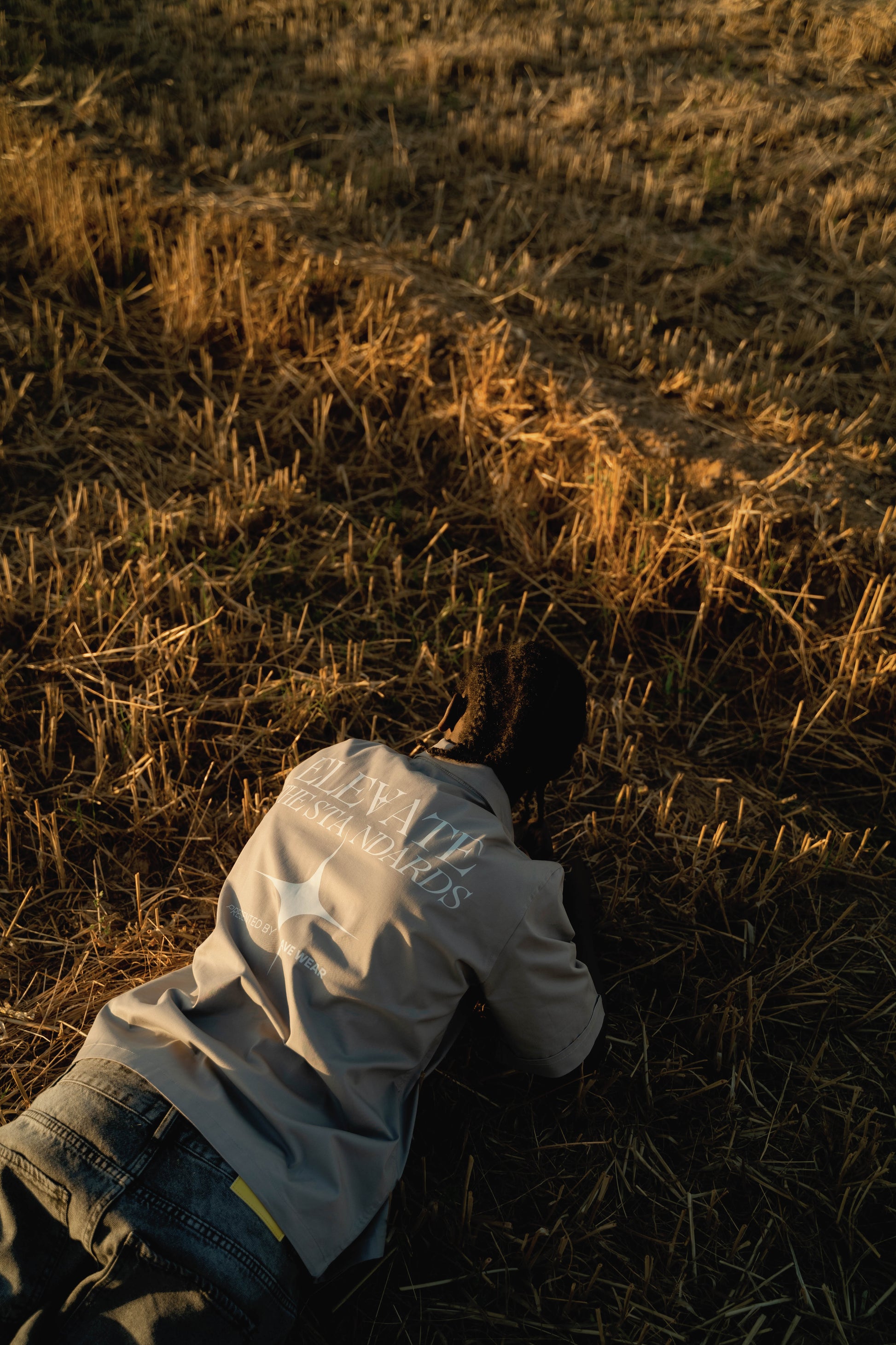 Person lying on a grassy field with a white plastic bag over their head at sunset.